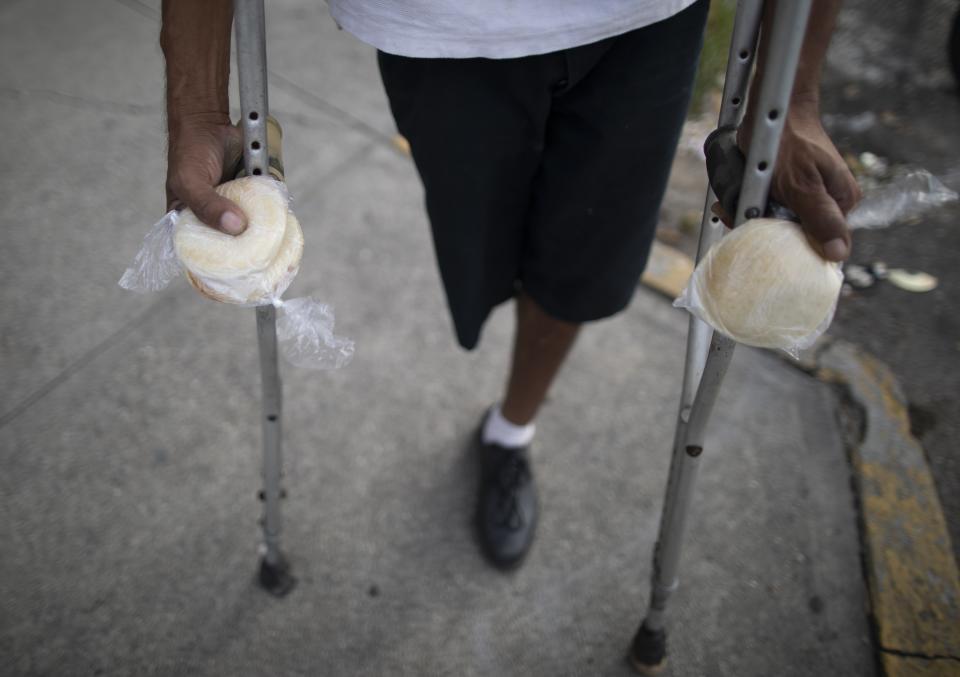 A man on crutches holds packages of homemade arepas given to him by 55-year-old publicist Andres Burgos, who started handing out the corn flour patties to needy children, adults and the elderly, in Caracas, Venezuela, Tuesday, Oct. 20, 2020. Burgos started small with his own money a year ago, passing out a few arepas on his bicycle route from home to the office, or in visits to nearby hospitals. (AP Photo/Ariana Cubillos)