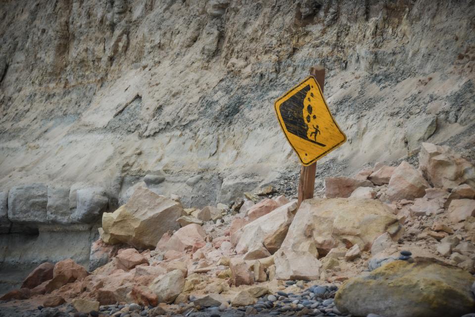 A warning sign sits on rubble at the base of coastal cliffs at Torrey Pines State Beach on Aug. 28.