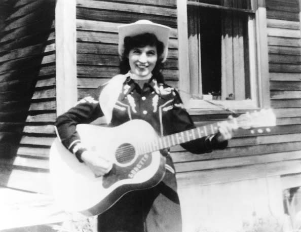 CIRCA 1960: Loretta Lynn holds her acoustic guitar as she poses for a portrait wearing a cowboy hat, a scarf and western shirt outside a log cabin in circa 1960. (Photo by Michael Ochs Archives/Getty Images)
