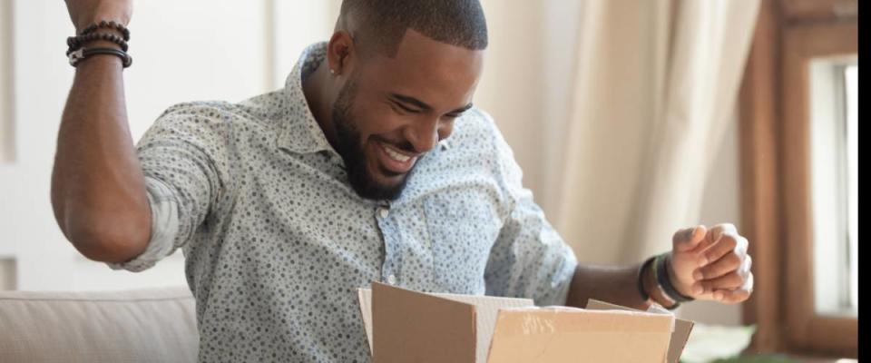 Excited african man customer receive good parcel open cardboard box at home satisfied with great purchase