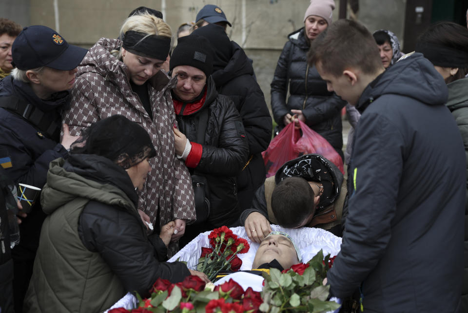 Family members of Vitaliy Alimov, his mother Maria, bottom left, and his wife Natalia, top second left, mourn over his body before his funeral in Bilhorod-Dnistrovskyi, Ukraine, Monday March 18, 2024. Alimov, a firefighter, was killed in the Russian attack on Odesa on Friday March 15. (AP Photo/Victor Sajenko)