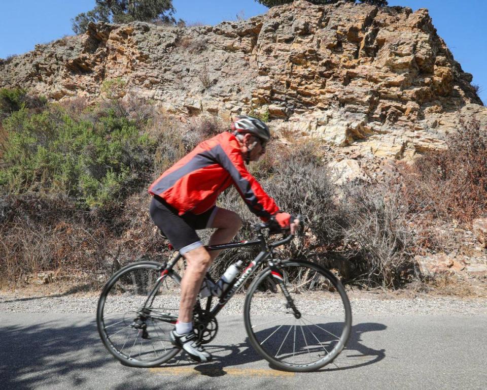 A cyclist glides by fossil-filled Monterey shale on the Bob Jones Trail on Sept. 22, 2023. The rocks were on the ocean floor about 14 million years ago, then uplifted to the surface by plate tectonics, according to a trail interpretive marker. The county wants to complete the trail from Avila Beach to San Luis Obispo but now will likely need to alter the route around at least one property whose owner has refused to sell a sliver of his land.