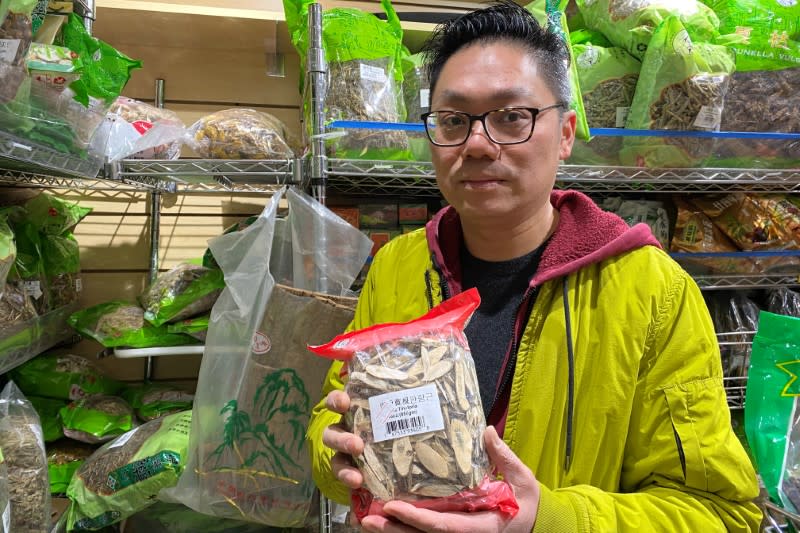 Patrick Siu, manager at Calihouse Nutrition holds a bag of isatis tinctoria root used in traditional Chinese medicine to treat respiratory illness in the Manhattan borough of New York City