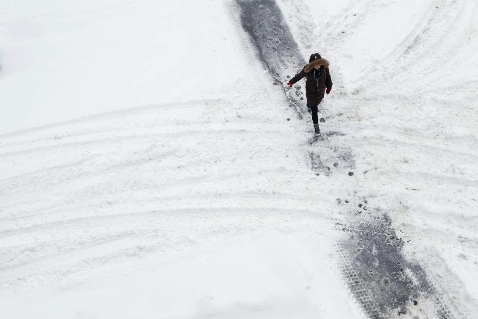 A woman walks along a path cleared in the snow while crossing a street in Ottawa