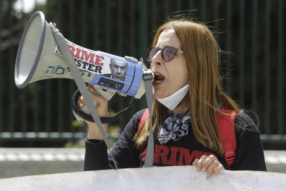 Israeli woman uses a bullhorn during a protest against Prime Minister Benjamin Netanyahu outside the national parliament in Jerusalem, Monday, March 23, 2020. The opposition has accused Netanyahu of using the coronavirus crisis as cover to undermine the country's democratic institutions. With the country in near-shutdown mode, Netanyahu has already managed to postpone his own pending criminal trial and authorize unprecedented electronic surveillance of Israeli citizens. (AP Photo/Sebastian Scheiner)
