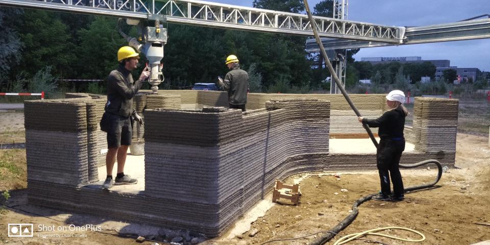 People standing near a tiny home as the 3D printer builds its walls.