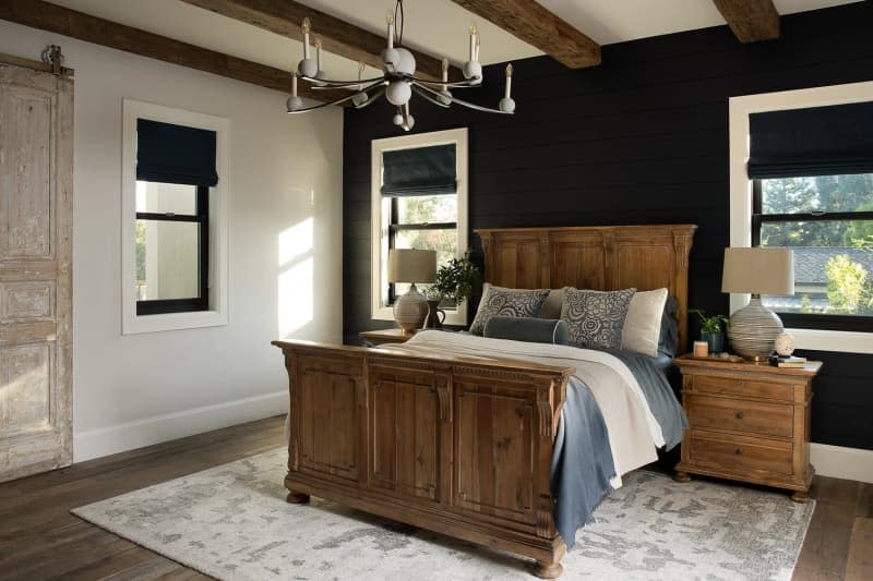 Bedroom with wood bed frame, black accent wall, and exposed wood beam ceiling