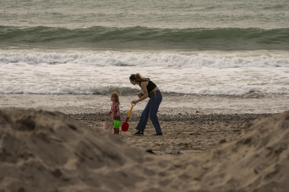 Babysitter Nathalie Miotti plays in the sand with Mia Seth, 2, on the beach behind a protective sand mound ahead of storms in Ventura, Calif., Wednesday, Jan. 31, 2024. (AP Photo/Damian Dovarganes)