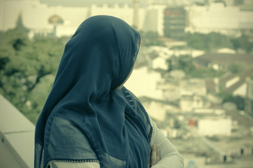 Pictured is a stock image of a woman in a dark blue hijab looking over a city.