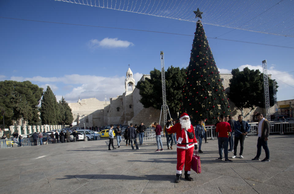 Un palestino disfrazado de Papá Noel da la bienvenida a los turistas que vistian la Iglesia de la Natividad, al fondo, en Belén el 5 de diciembre del 2019. (AP Photo/Majdi Mohammed)