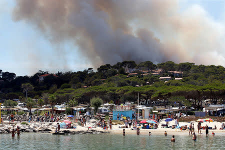 Smoke fills the sky above a burning hillside as tourists swim in the waters off the beach in Bormes-les-Mimosas, in the Var department, France, July 26, 2017. REUTERS/Jean-Paul Pelissier