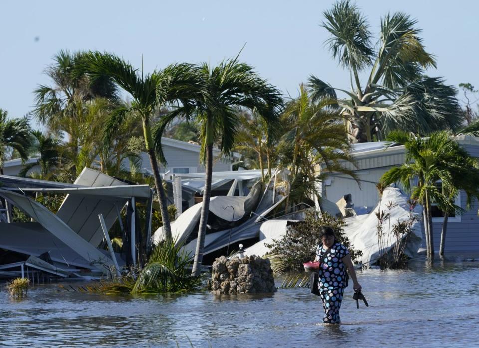 A person walks in a flooded area in front of a wrecked home.