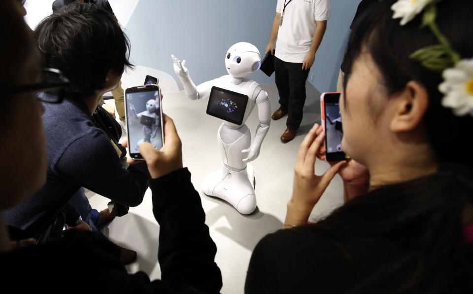 People take pictures of SoftBank Corp's human-like robots named 'pepper' displayed at its branch in Tokyo