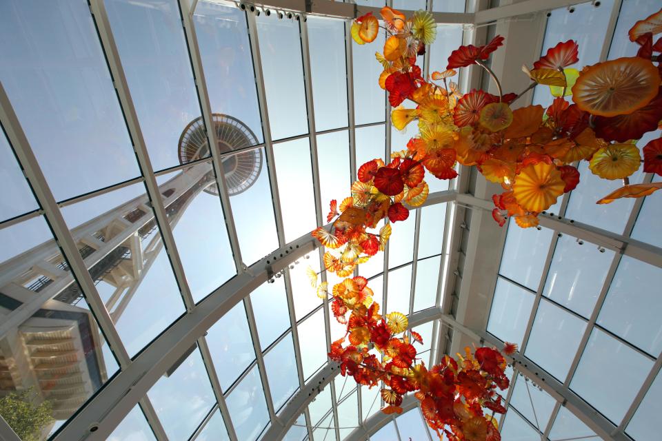 FILE - In this May 17, 2012 photo, the Space Needle is seen through the walls and ceiling of the "Glasshouse," featuring a 100-foot suspended, 1,340-piece sculpture, during a preview of the Chihuly Garden and Glass exhibit at the Seattle Center in Seattle.   Fifty years after the World's Fair inserted the Space Needle into Seattle's skyline, the city is celebrating that anniversary by offering an array of new things to see and do at Seattle Center: from a zip line to the new art glass museum.  (AP Photo/Elaine Thompson)