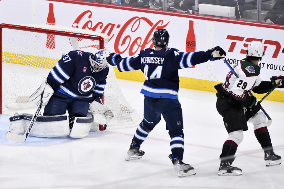 Winnipeg Jets goaltender Connor Hellebuyck (37) makes a save on a shot as Josh Morrissey (44) hooks Arizona Coyotes' Barrett Hayton (29) during the first period of an NHL hockey game, Tuesday, March 21, 2023 in Winnipeg, Manitoba. (Fred Greenslade/The Canadian Press via AP)