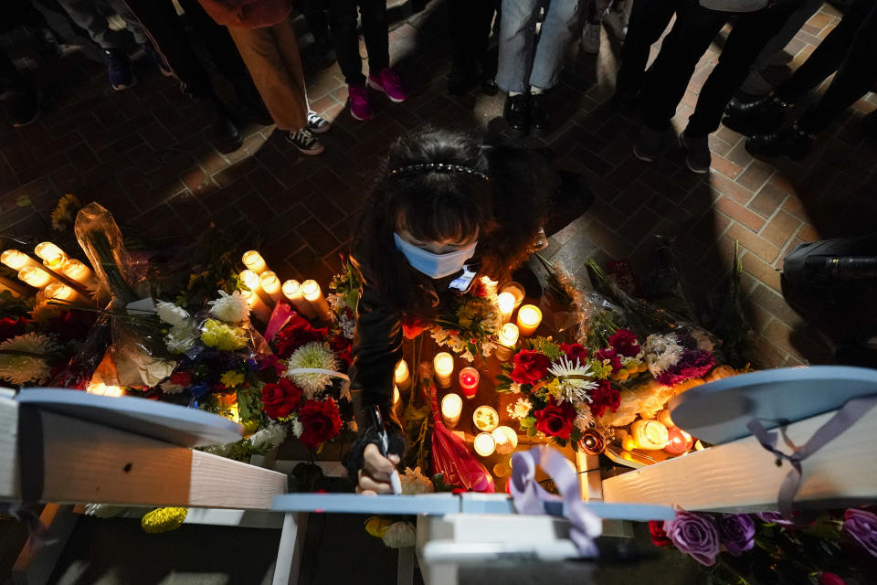 A woman writes a message on a wooden heart that displays the name of a victim at a vigil outside Monterey Park City Hall, blocks from the Star Ballroom Dance Studio, late Tuesday, Jan. 24, 2023, in Monterey Park, Calif. A gunman killed multiple people at the ballroom dance studio late Saturday amid Lunar New Year's celebrations in the predominantly Asian American community. (AP Photo/Ashley Landis)