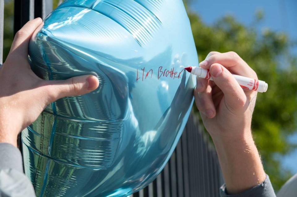 A young man writes “LYM Brother” on a blue balloon that is part of the memorial in front of the Ethan Apartments in Arden Arcade on Tuesday honoring a 15-year-old shooting victim. A 20-year-old victim, who was inside an apartment, survived.