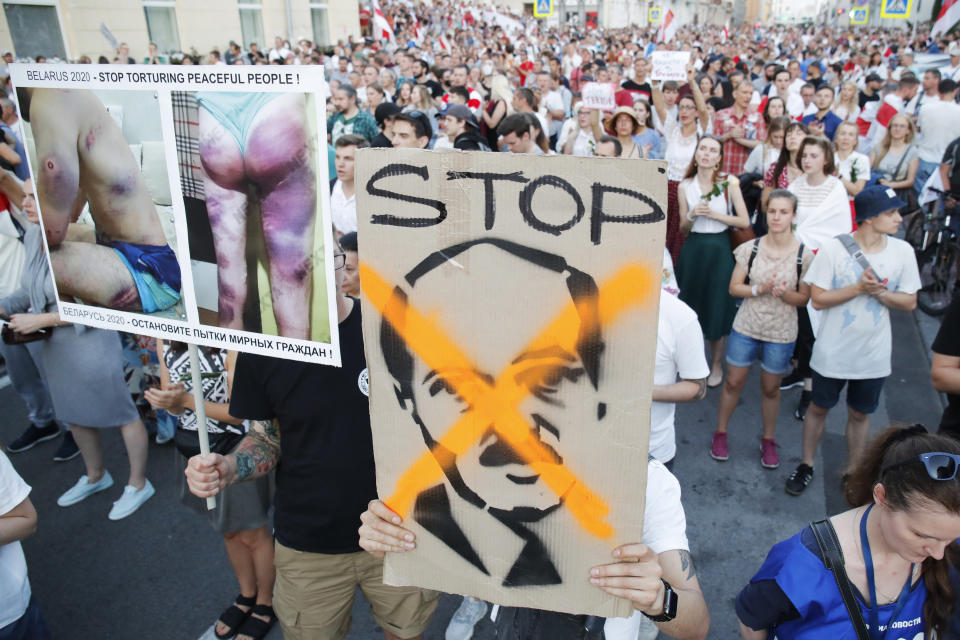 People carry a poster showing photos of protesters allegedly beaten by police, left, and a caricature depicting Belarusian President Alexander Lukashenko, center, during an opposition rally in Minsk, Belarus, Monday, Aug. 17, 2020. Belarusian President Alexander Lukashenko said the country could only have a new presidential election after approving an amended version of its constitution, in an apparent bid to buy some time amid the growing political crisis. (AP Photo/Dmitri Lovetsky)