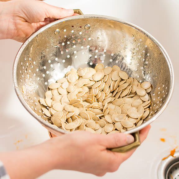 Rinsed pumpkin seeds in a strainer over a white sink