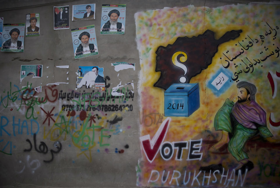 In this Wednesday, March 12, 2014 photo, Afghan election campaign placards are placed on a wall next to a huge graffiti urging people to go to the polls in Kandahar, southern Afghanistan. Warlords with a violent past have played a role in influencing Afghan politics since a U.S.-led coalition helped oust the Taliban in 2001. But they are emerging to play an overt political role in next month’s presidential elections as President Hamid Karzai leaves the scene. (AP Photo/Anja Niedringhaus)