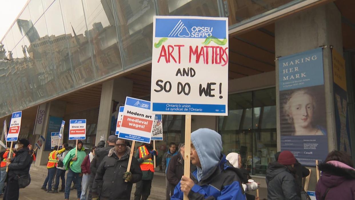 Workers from the Art Gallery of Ontario hold various signs as they begin their first day of strike action on Tuesday. (CBC - image credit)