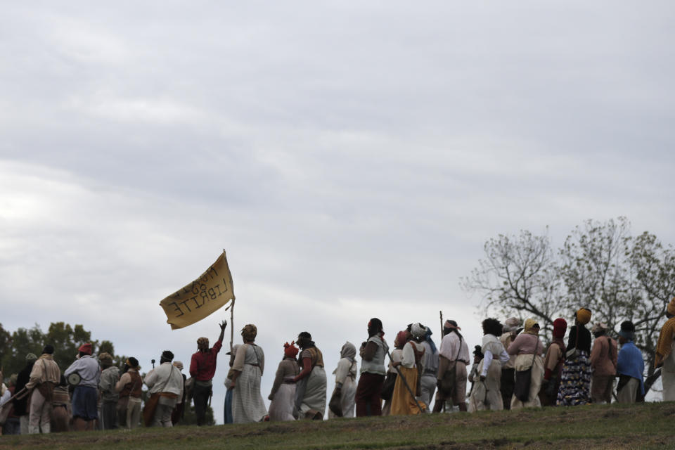 People march along the Mississippi River levee as they participate in a reenactment of the largest slave rebellion in U.S. history, in LaPlace, La., Friday, Nov. 8, 2019. The reenactment was conceived by Dread Scott, an artist who often tackles issues of racial oppression and injustice. (AP Photo/Gerald Herbert)