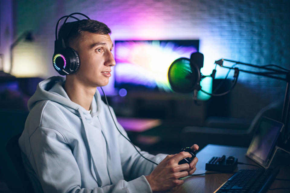 Man in hoodie using computer and gaming equipment, focused on screen