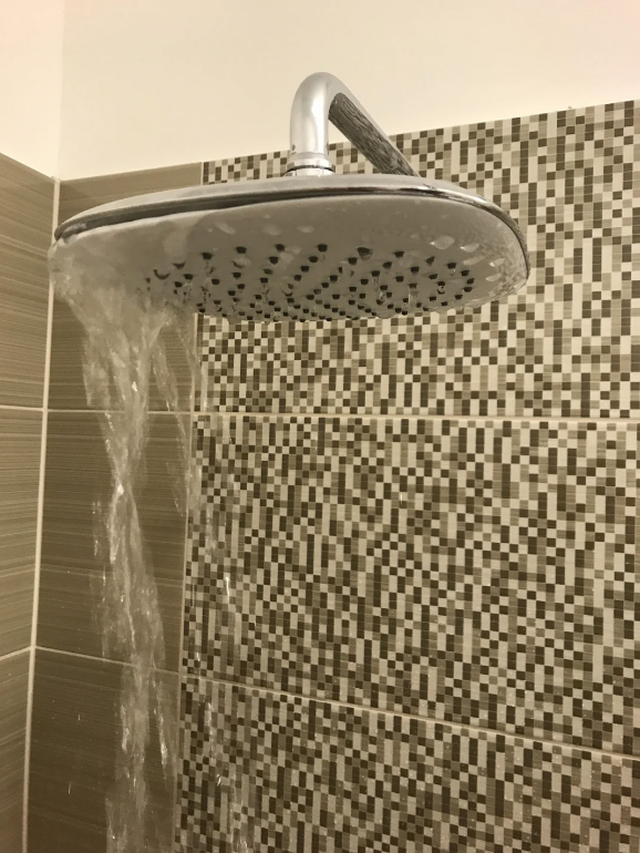 Water flows from a showerhead in a bathroom with a tile wall pattern