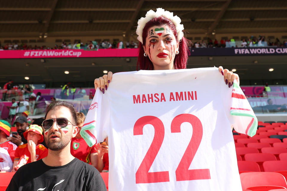 oDOHA, QATAR - NOVEMBER 25: A female Iran fan holding the a shirt for Mahsa Amini who was killed by police brutality during the FIFA World Cup Qatar 2022 Group B match between Wales and IR Iran at Ahmad Bin Ali Stadium on November 25, 2022 in Doha, Qatar. (Photo by Robbie Jay Barratt - AMA/Getty Images)