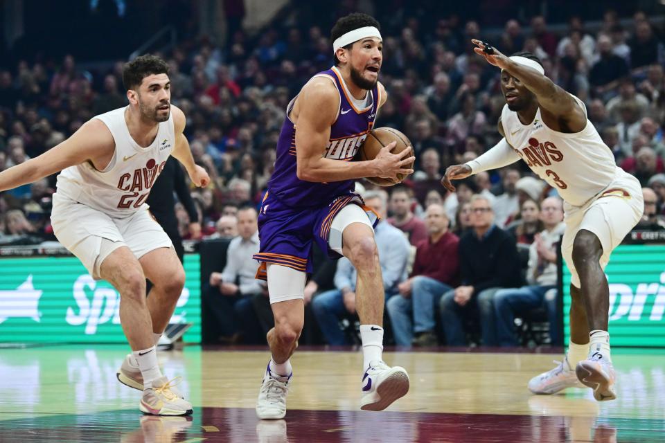 Phoenix Suns guard Devin Booker (1) drives to the basket between Cleveland Cavaliers forward Georges Niang (20) and guard Caris LeVert (3) during the first half at Rocket Mortgage FieldHouse in Cleveland on March 11, 2024.