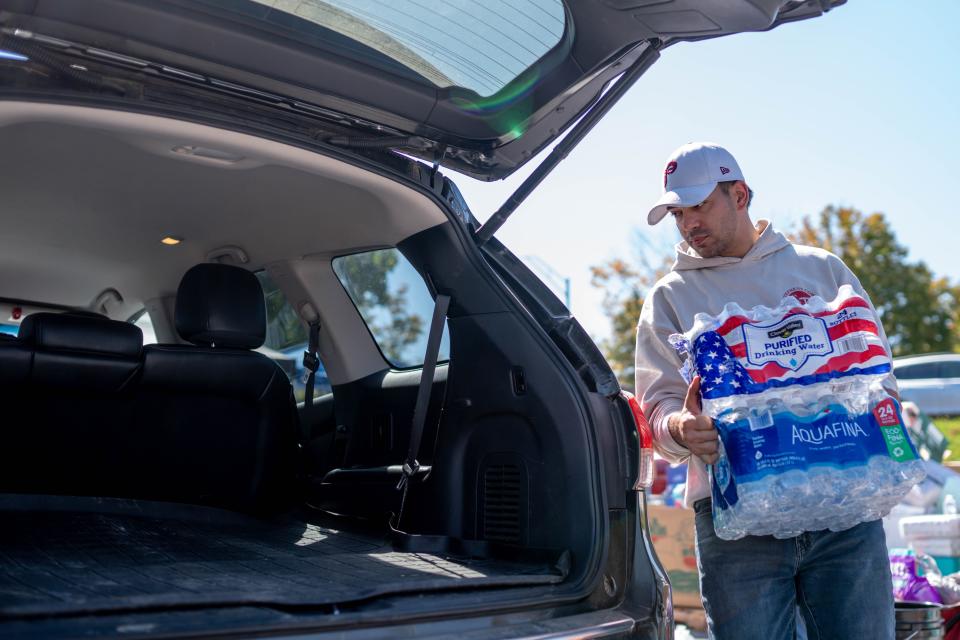 Oct 5, 2024; Asheville, NC, USA; Chris Mueller carries waters to a trunk as MANNA FoodBank provide resources to residents at the WNC Farmers Market during the aftermath of flooding caused by the remnants of Hurricane Helene. Mandatory Credit: Nathan Fish-USA TODAY