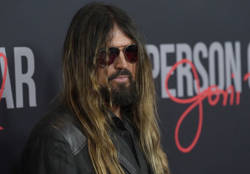 A man with long brown hair and a beard wearing sunglasses and a leather jacket