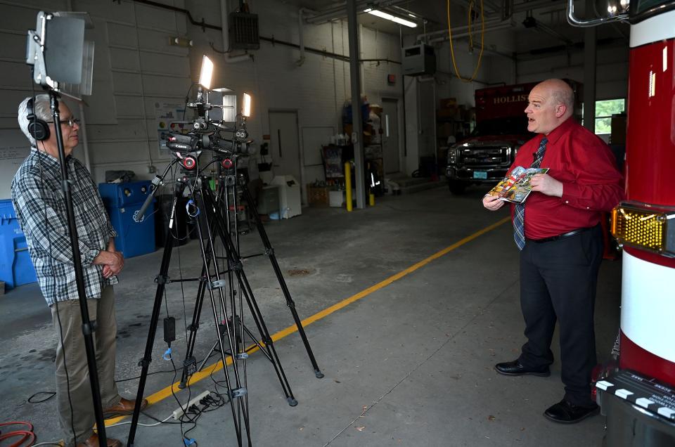 Holliston Fire Chief Michael Cassidy, right, tapes his reading of "Firefighter Nozzelhead Goes to Mexico" for Holliston Cable Access Television (HCAT) station manager Bruce GIlfoy, left, at the Central Street fire station, May 25, 2022. The program is called "Story Time with Chief Cassidy."
