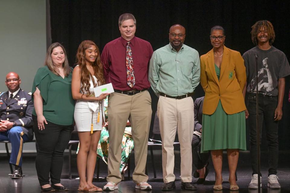 Spencer High School senior Alexia Hill holds the envelope containing the $1,000 Alexis McRae Scholarship she received during the senior class awards ceremony May 8, 2024, in the Spencer auditorium. Standing with Alexia, from left, are Alexis’ parents, Katy and Michael, and retired Spencer principal Johnny Freeman, who established and funded the scholarship to memorialize Alexis, who was a 15-year-old student at Rainey McCullers School of the Arts when she died in Feburary from osteosarcoma. Michael McRae is a math coach at Spencer.