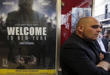 A man stands next to a poster of the film "Welcome to New York" directed by Abel Ferrara at a movie theatre ahead of a premiere screening during the 67th Cannes Film Festival in Cannes May 17, 2014. REUTERS/Eric Gaillard