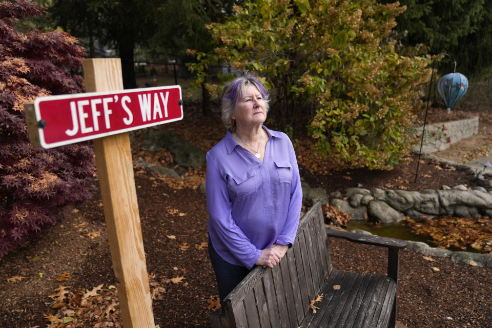 Lynn Wencus, of Wrentham, Mass., stands near a sign and bench placed in a garden in memory of her son Jeff at her home, in Wrentham, Tuesday, Nov. 7, 2023. Wencus lost Jeff to a heroin overdose in 2017. Families who lost loved ones to overdose are divided over OxyContin maker Purdue Pharma's plan to settle lawsuits over the toll of opioids with governments. It could provide billions to address an overdose epidemic and pay some victims. But it would also protect members of the Sackler family who own the company from future lawsuits. (AP Photo/Steven Senne)
