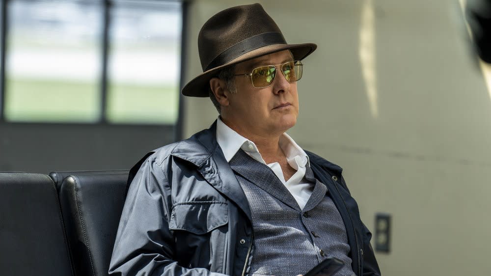  James Spader as Raymond Reddington sitting at an airport in a hat and sunglasses in The Blacklist 