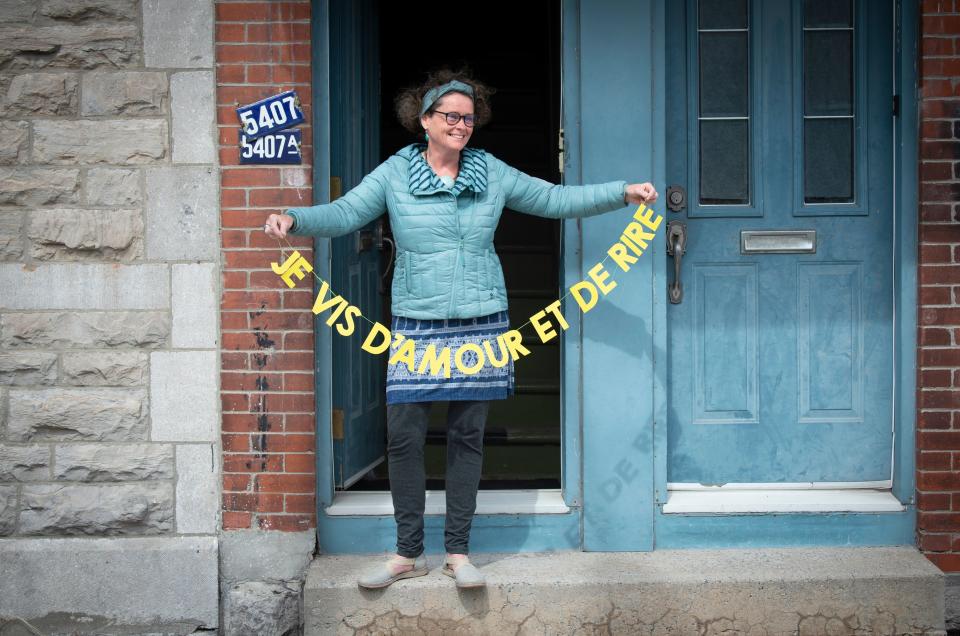 Valerie Menguy holds her banner "I live on love and laughter" by artist Patsy Van Roost on May 6, 2020, in Montreal. - Artist Patsy Van Roost is brightening up Montreal balconies and putting smiles on pandemic-weary passers-by with a litany of personalized messages on multicolored banners hung across the city. "The idea is to spread a little love for people during their solo walks," she told AFP. (Photo by Sebastien St-Jean / AFP) (Photo by SEBASTIEN ST-JEAN/AFP via Getty Images)