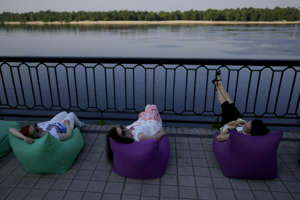 Women rest in front of the Dnieper River in Kyiv, Ukraine, Friday, June 10, 2022. With war raging on fronts to the east and south, the summer of 2022 is proving bitter for the Ukrainian capital, Kyiv. The sun shines but sadness and grim determination reign. (AP Photo/Natacha Pisarenko)