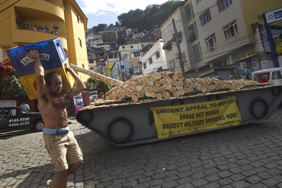 A worker carries crates past a fake life-sized war tank covered with bread sitting on display in the Santa Marta slum as part of a "Bread not Bombs" protest on the sidelines of the Rio+20 UN Conference on Sustainable Development in Rio de Janeiro, Brazil, Tuesday, June 19, 2012. Activists placed the fake war tank covered with bread for residents to eat and to demand leaders at the Rio+20 to redirect military spending to pay for basic needs. (AP Photo/Silvia Izquierdo)
