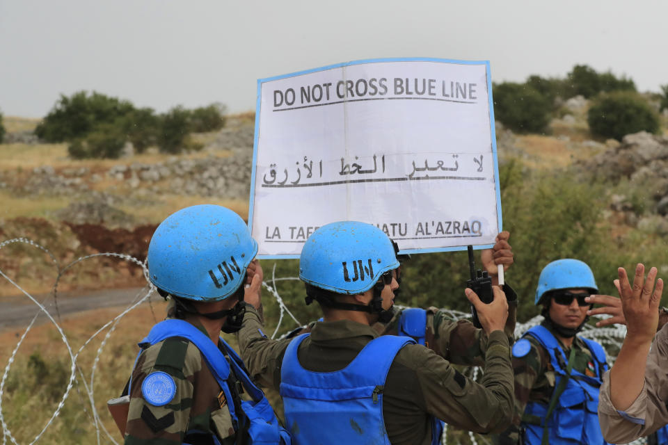 U.N. peacekeepers carrying a banner in Arabic, English and French to urge protesters not to cross the border line on the outskirts of the southern Lebanese village of Kfar Chouba, south Lebanon, Friday, June 9, 2023. Israeli soldiers fired tear gas to disperse scores of protesters who pelted the troops with stones along the border with Lebanon Friday, leaving some Lebanese demonstrators and troops suffering breathing problems. (AP Photo/Mohammad Zaatari)