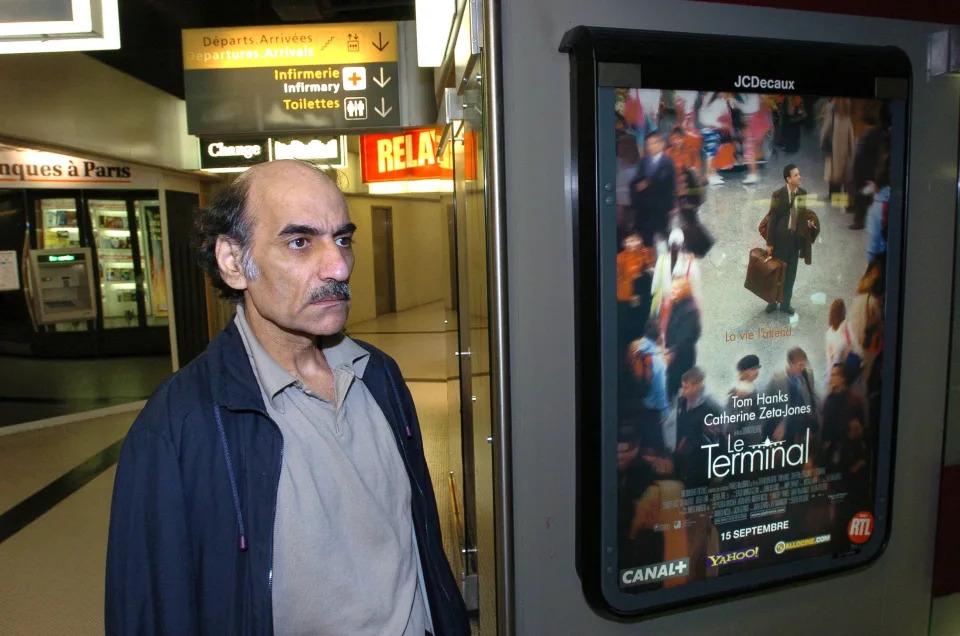 (FILES) In this file photo taken on August 12, 2004 Mehran Karimi Nasseri passes by the poster of the movie inspired by his life, in the terminal 1 of Paris Charles De Gaulle airport. - Mehran Karimi Nasseri, a political refugee who lived over 18 years in Paris' Roissy-Charles de Gaulle airport and inspired director Steven Spielberg's "The Terminal", died, aged 77, at Roissy-Charles de Gaulle airport's terminal 2F, as reported to AFP by airport officials.