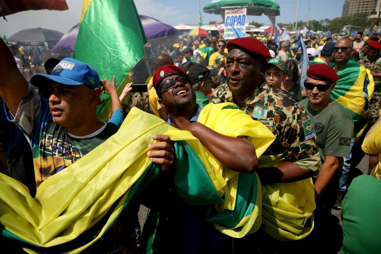 Men in red berets join other people carrying a large swath of yellow-and-green cloth