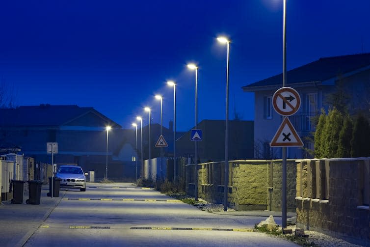 A residential street with a row of lamp posts shining white light.