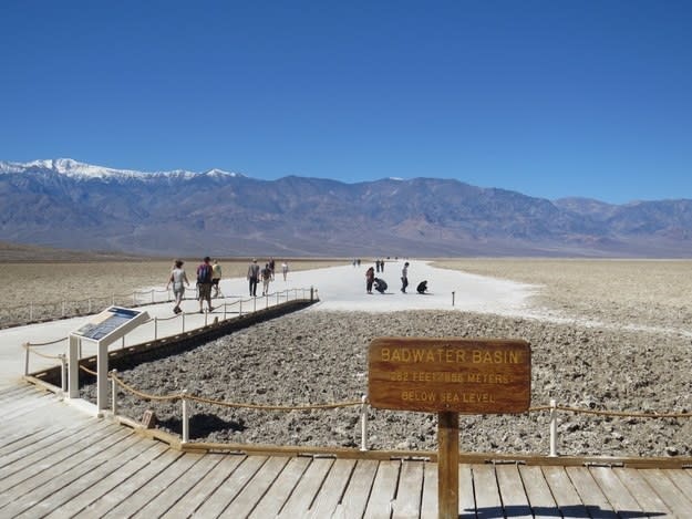 A flat and desolate desert landscape has people walking over a boardwalk.