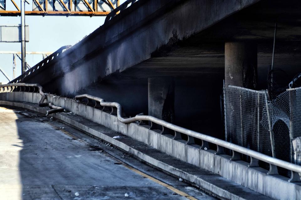 Smoke continues to billow from Interstate 10 as an off ramp is seen with a melted railing and burn scars after it was severely damaged by a large fire near downtown Los Angeles on Saturday, Nov. 11, 2023. Authorities say firefighters have mostly extinguished the large blaze that burned trailers, cars and other things in storage lots beneath a major highway near downtown Los Angeles, forcing the temporary closure of the roadway. (AP Photo/Richard Vogel)