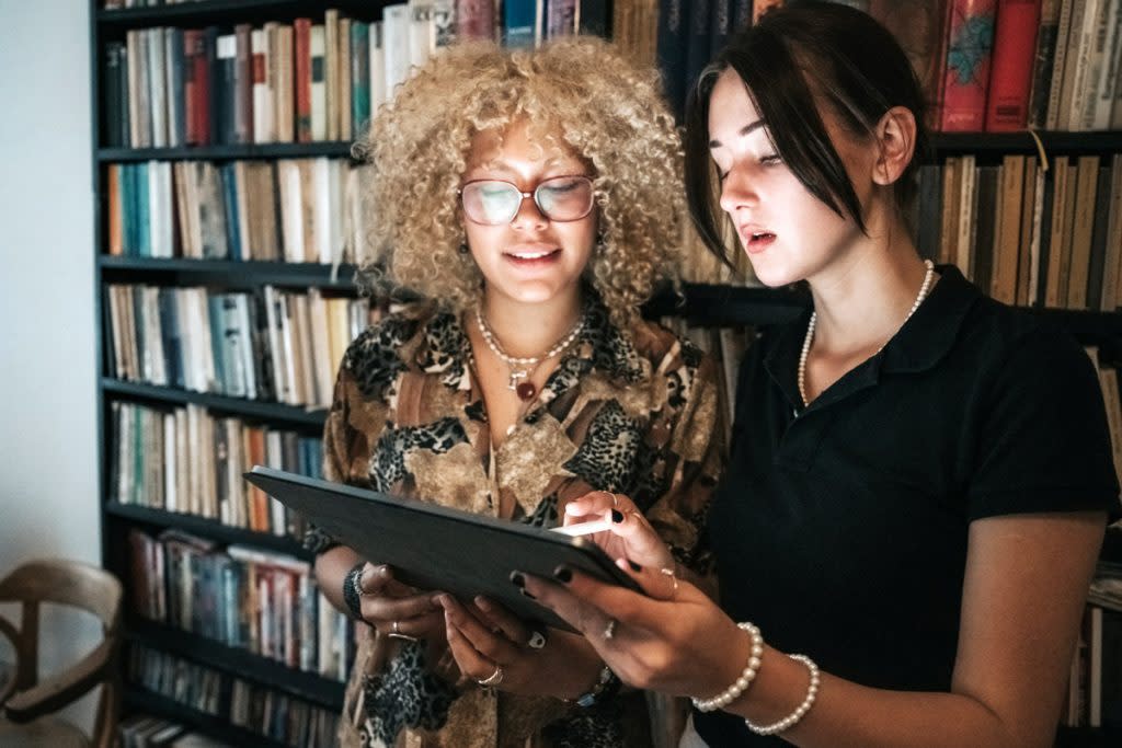 Two women look at a tablet in a library.