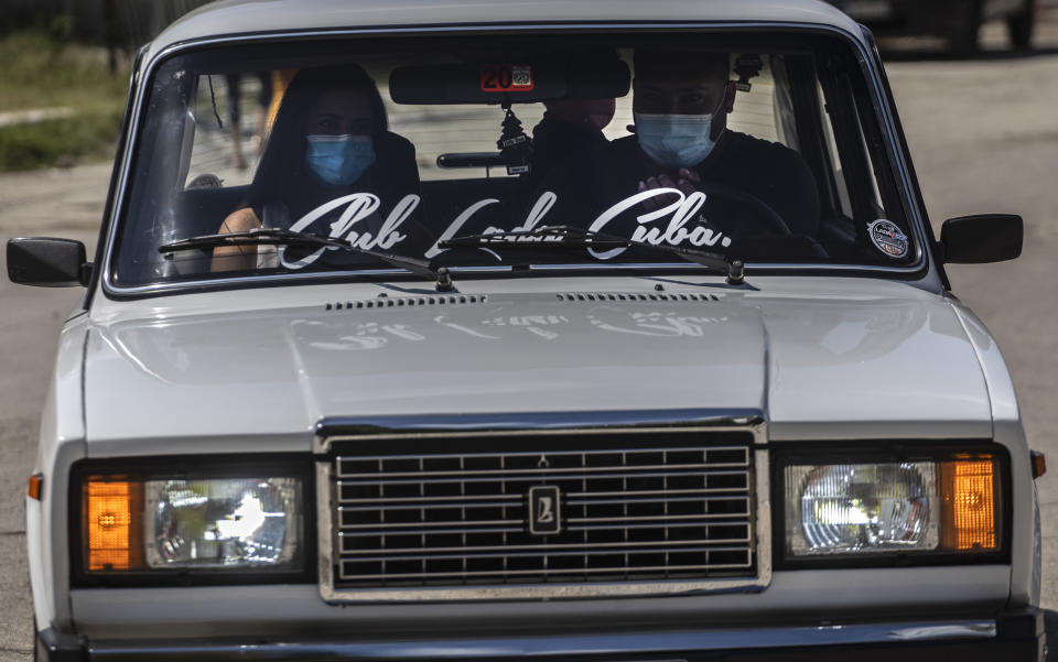 A family wearing masks against the spread of the new coronavirus travel in a Soviet-era Lada car during the Lada Cuba Club meeting in Havana, Cuba, Sunday, March 21, 2021. At the end of the 1950s, Cuba was one of the countries with the highest number of vehicles per inhabitants. (AP Photo/Ramon Espinosa)