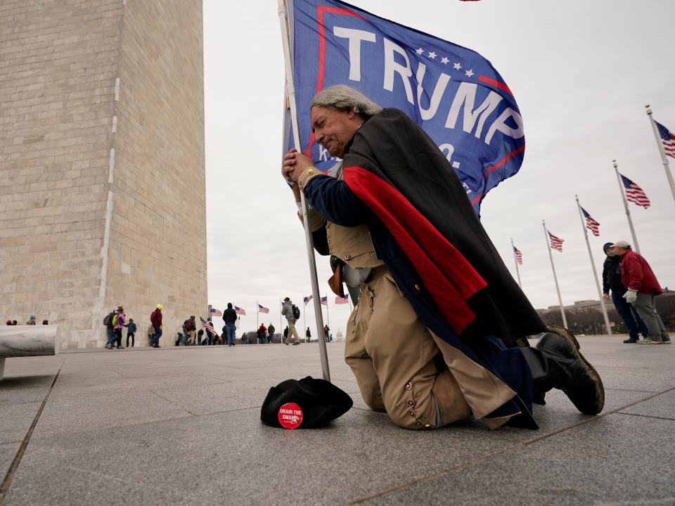 A man dressed as George Washington kneels and prays near the Washington Monument with a Donald Trump flag on Wednesday, Jan. 6, 2021, in Washington, DC.