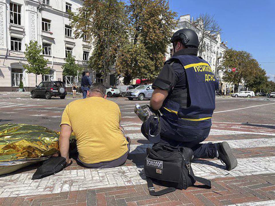 In this photo provided by the Ukrainian Emergency Service, a man sits near a covered dead body after Russian attack in Chernihiv, Ukraine, Saturday, Aug. 19, 2023. (Ukrainian Emergency Service via AP)